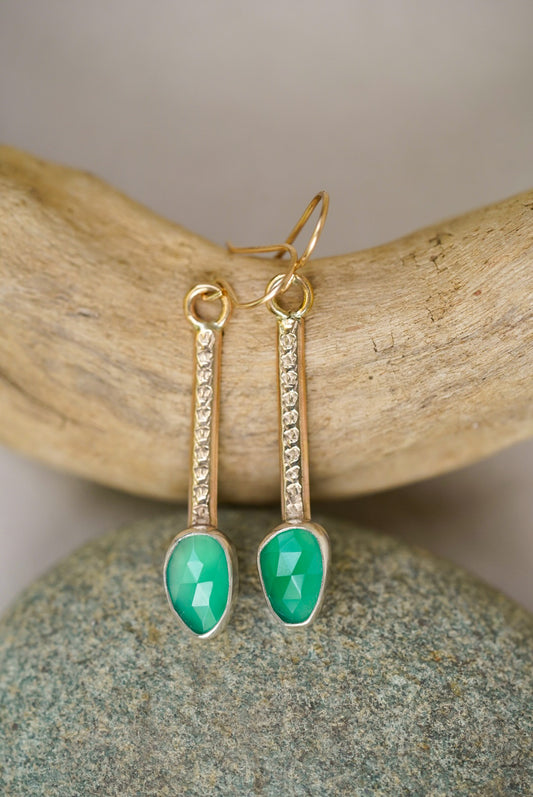 Gold earrings with green gemstones on a natural stone background