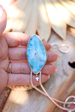 Load image into Gallery viewer, Teardrop-shaped blue stone pendant on a chain held by a hand with a blurred natural background