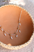 Load image into Gallery viewer, Necklace with pearls and gold accents on a textured surface