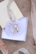 Load image into Gallery viewer, white jewelry ox with a hanging sun tag holding a Gold necklace with pearl, opal and starburst shape pendants on a beige surface