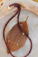 Load image into Gallery viewer, Two necklaces, one with gold beads and the other with red beads, on a stone surface.