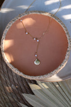 Load image into Gallery viewer, A gold lariat style necklace with lustrous pearls and a gold shell detail, displayed on a woven mat.