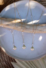 Load image into Gallery viewer, A gold lariat style necklaces with lustrous pearls and a gold shell detail, displayed on a beige tray.