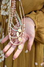 Load image into Gallery viewer, Hand holding multiple beaded necklaces with a blurred floral and mustard background