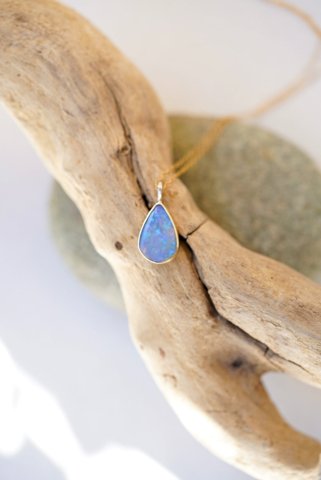 Opal pendant necklace on a piece of driftwood with a blurred background