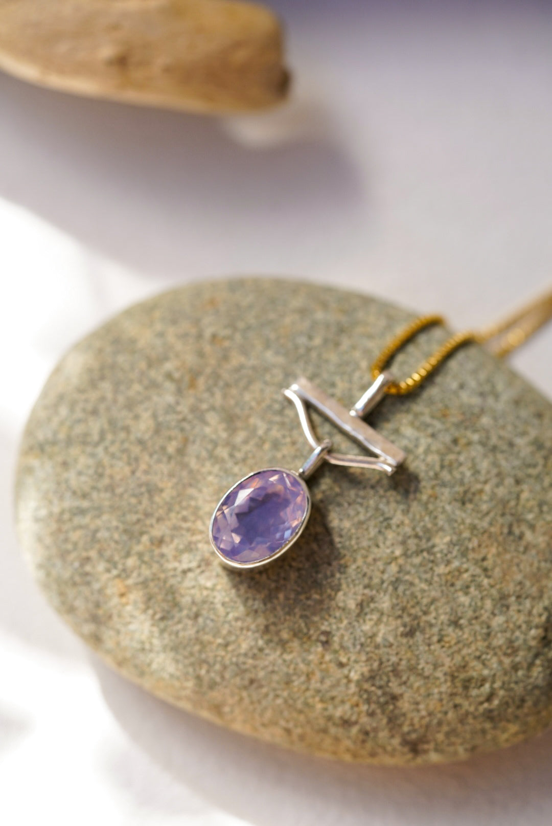 Purple gemstone pendant on a gold chain resting on a rock
