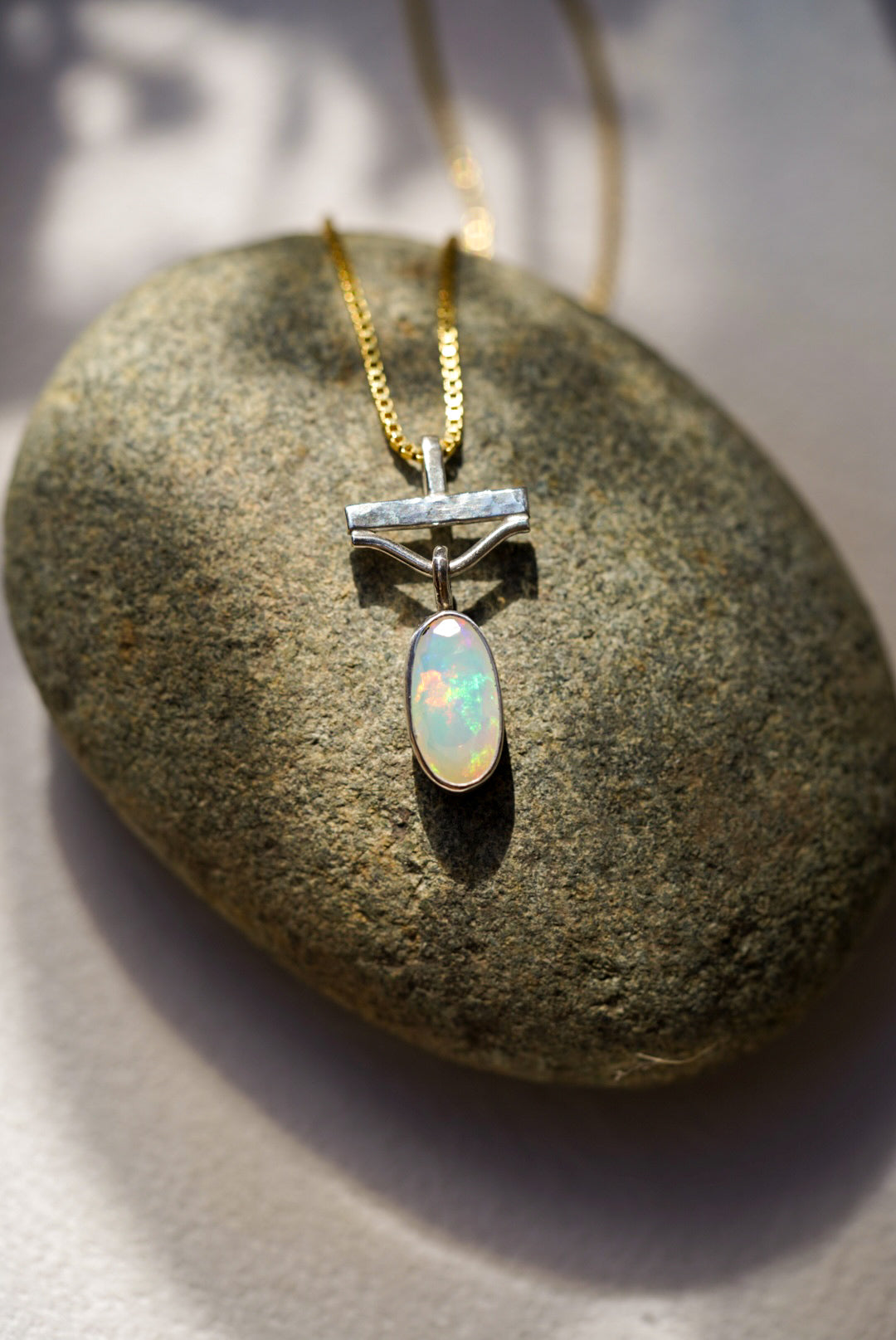 Opal pendant on a gold chain resting on a stone surface