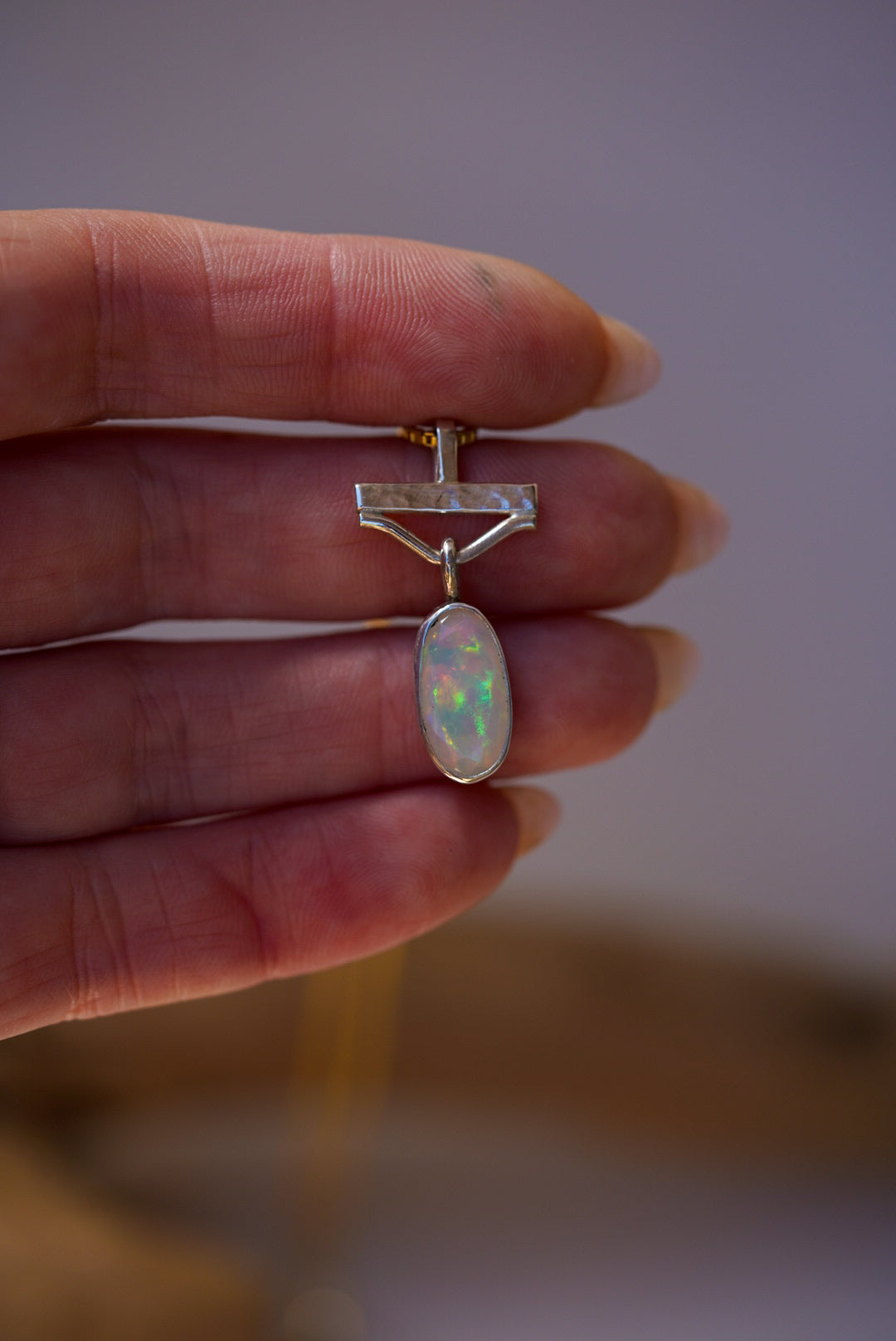 Opal pendant held between fingers against a neutral background