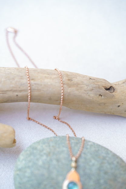 Close-up of the hair on a green pendant with gold temple design on a piece of driftwood 
