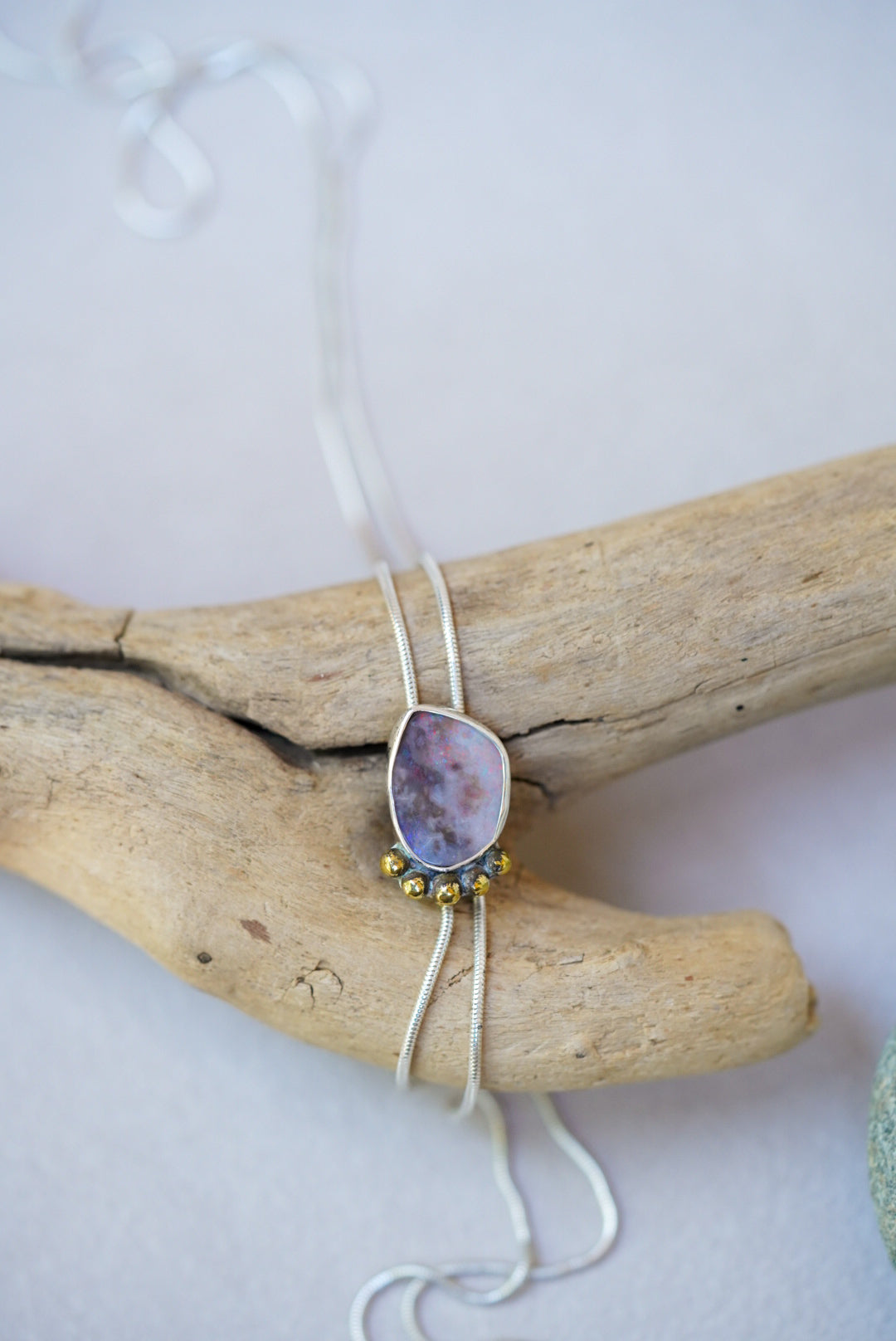 Opal bolo necklace on a piece of driftwood on a white background