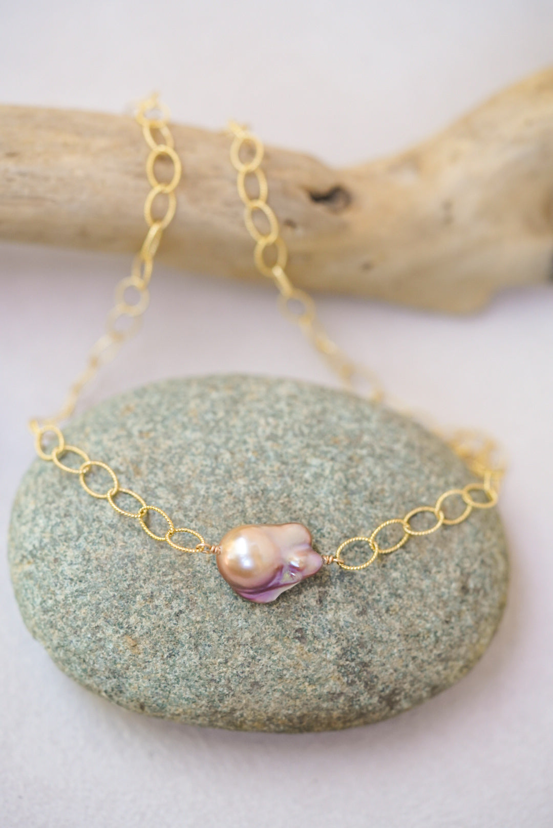 Gold chain necklace with a pink pearl pendant on a green stone