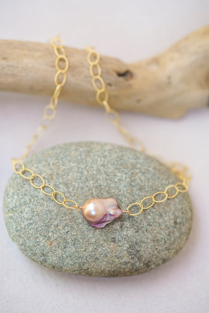 Gold chain necklace with a pink pearl pendant on a green stone