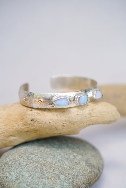 Silver bracelet with opal stones on a stack of pebbles