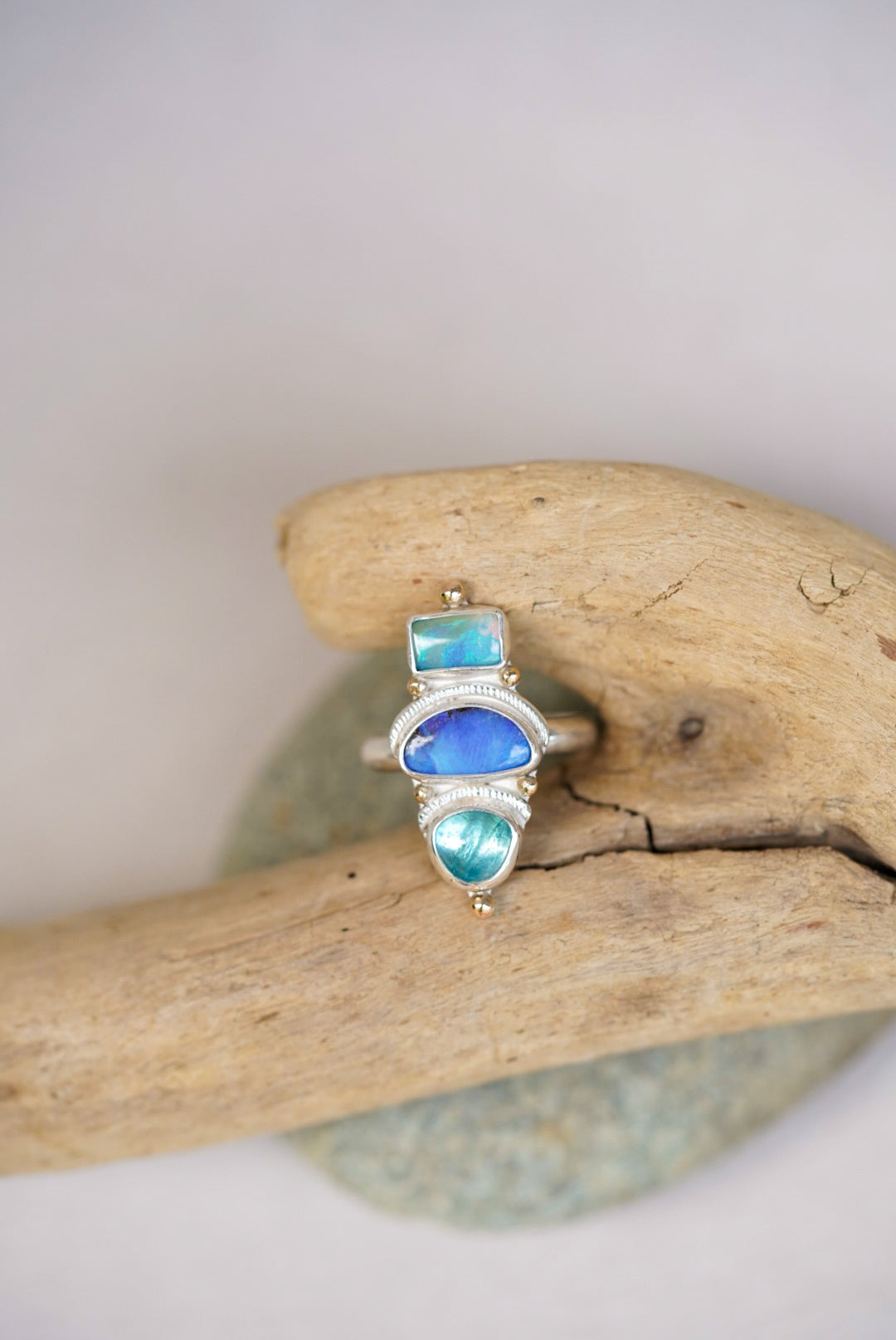 Silver ring with blue and green gemstones on a piece of driftwood.