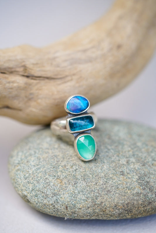 Silver ring with blue and green gemstones on a stone surface