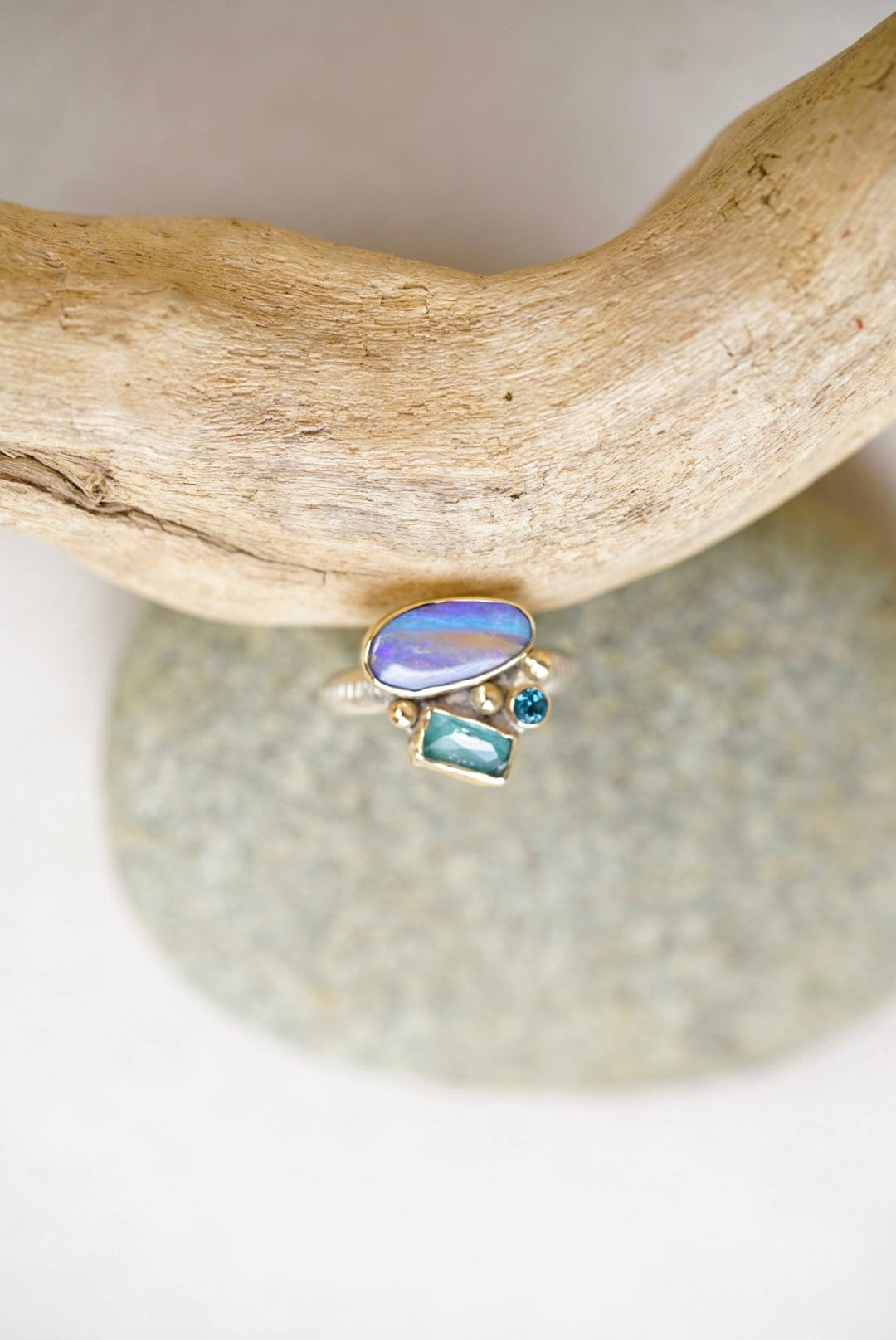 Ring with opal and blue gemstones on a piece of driftwood