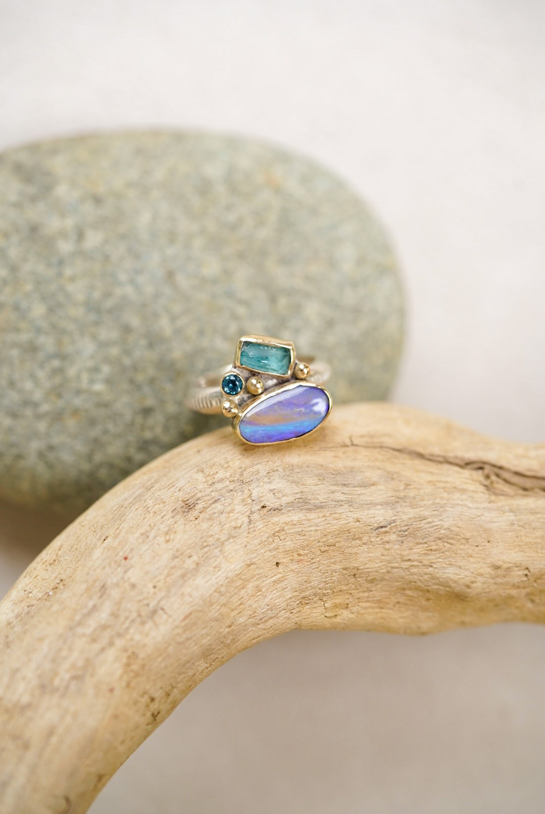 Ring with opal and blue gemstones on a piece of driftwood