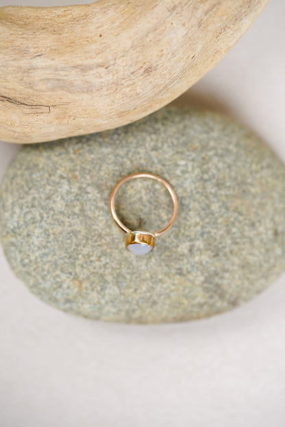 Light purple chalcedony stone with gold ring on a rock next to driftwood