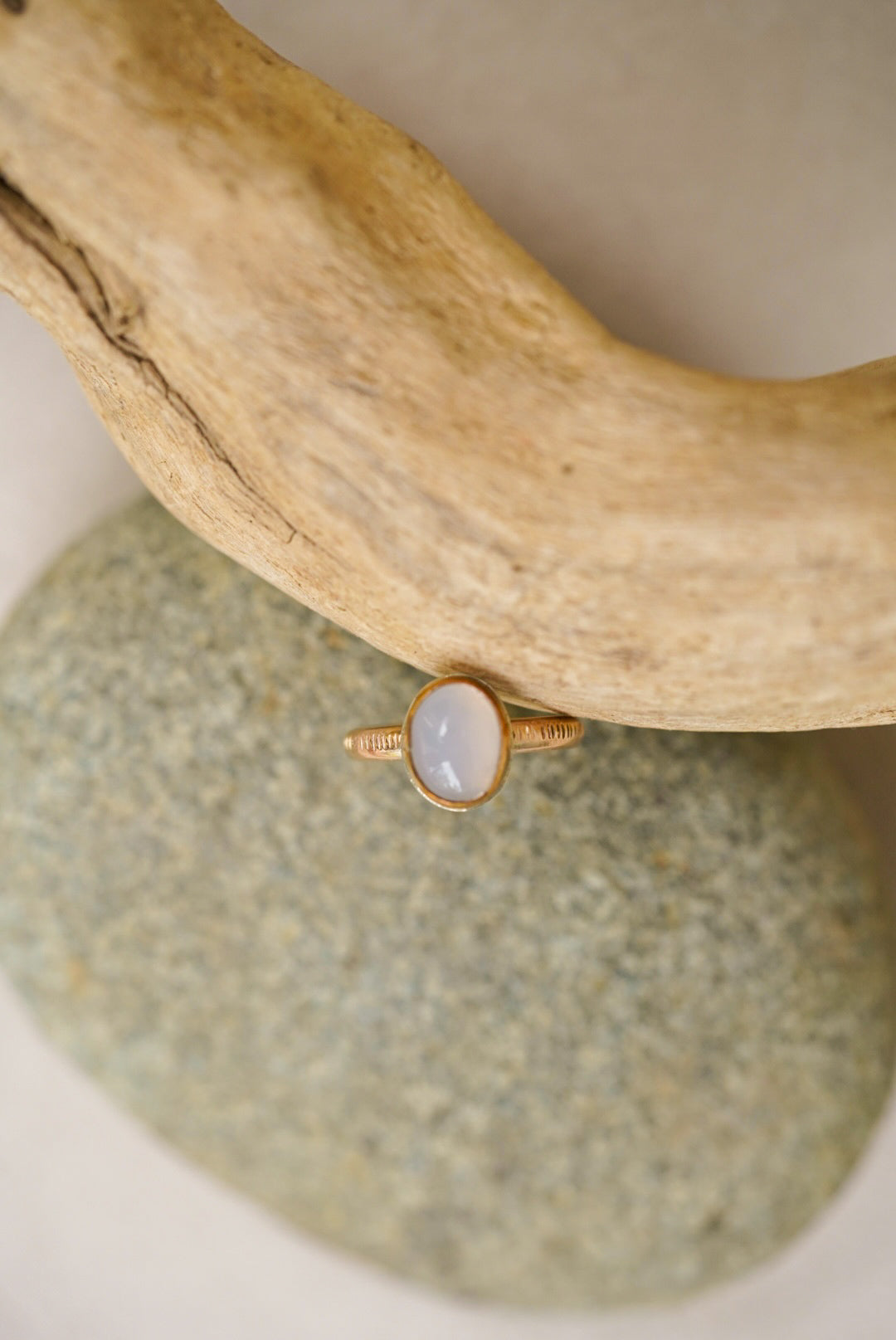 Light purple chalcedony stone with gold ring on a rock next to driftwood