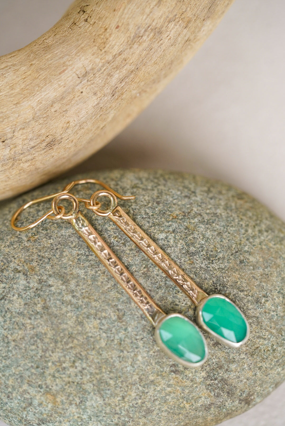 Gold earrings with green stones on a stone surface