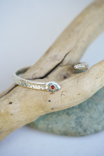 Silver cuff with a red stone on a piece of driftwood