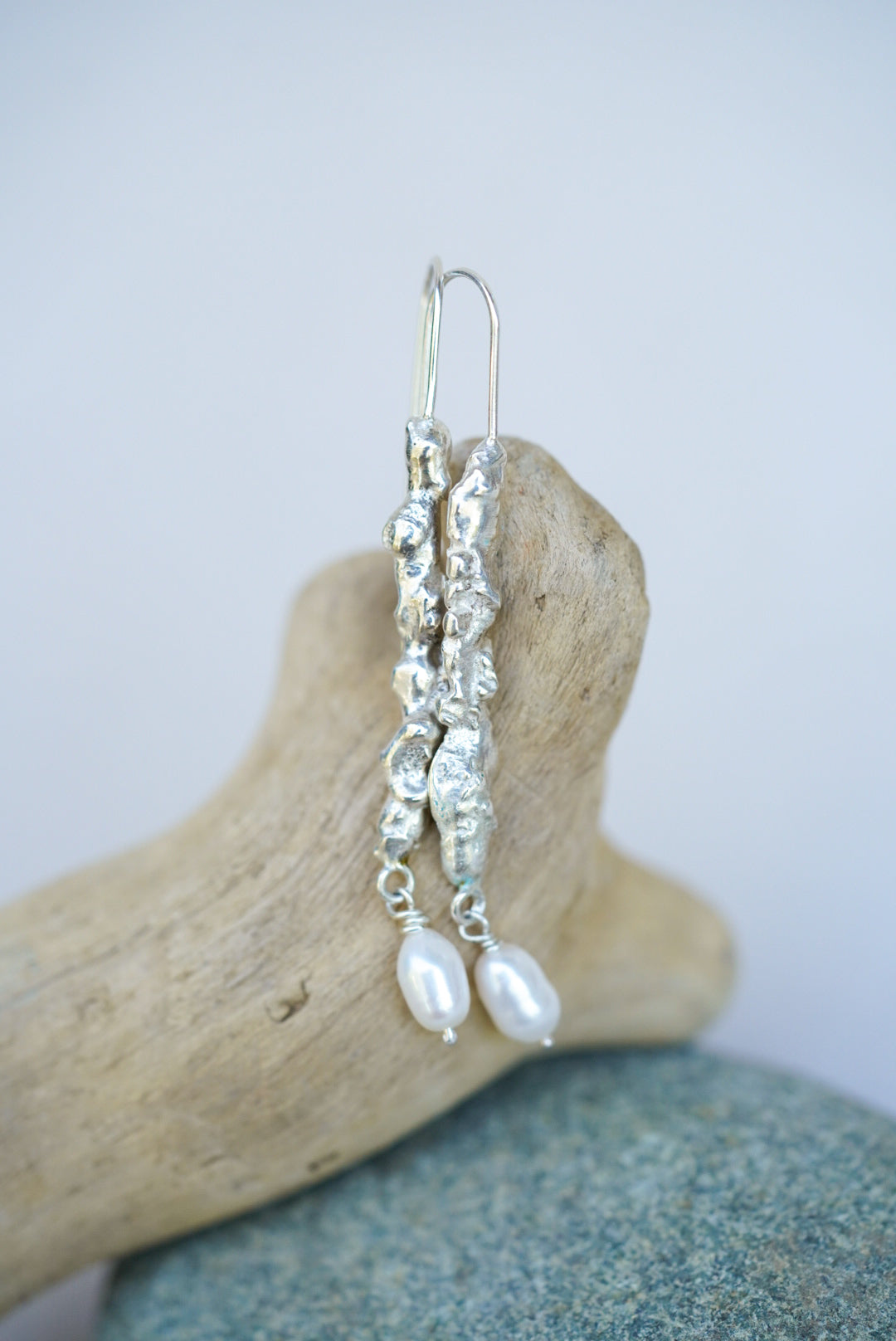 Silver earrings with pearls on a piece of driftwood against a light background