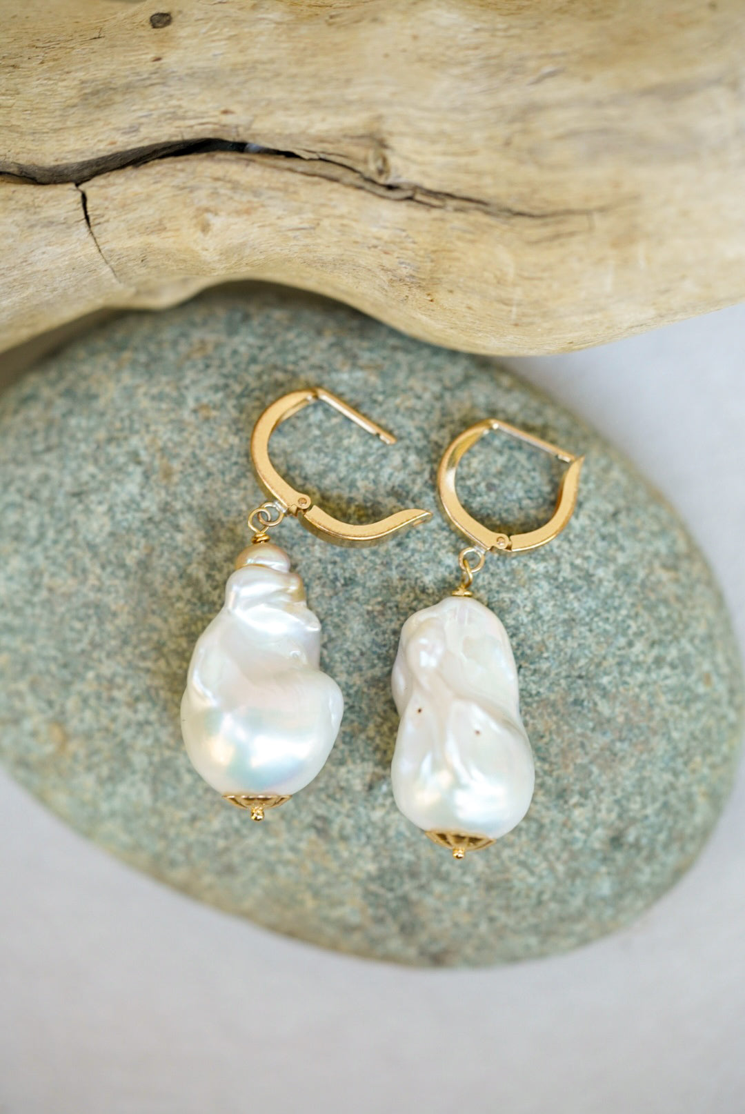 Pearl earrings with gold hooks on a stone surface