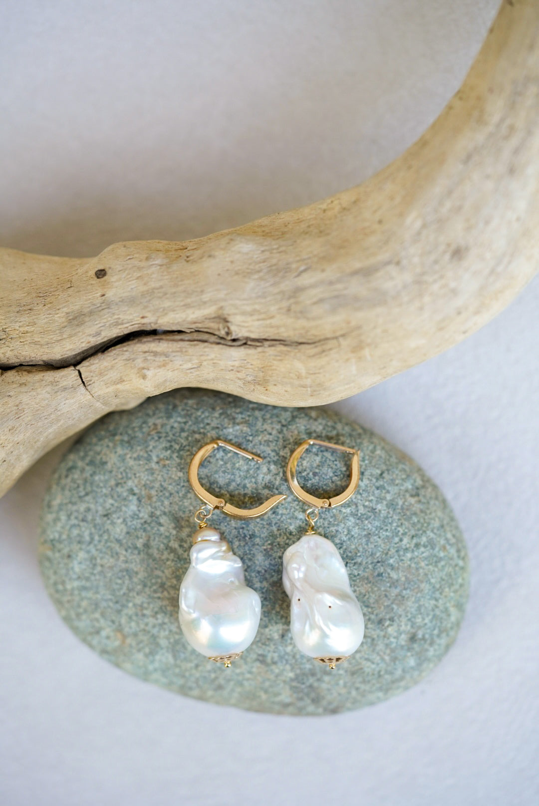 Pair of pearl earrings on a stone with driftwood in the background