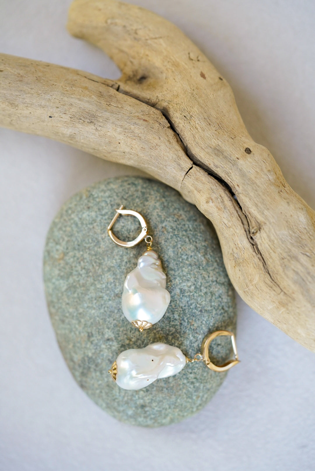 Pearl earrings with gold accents on a stone surface with driftwood