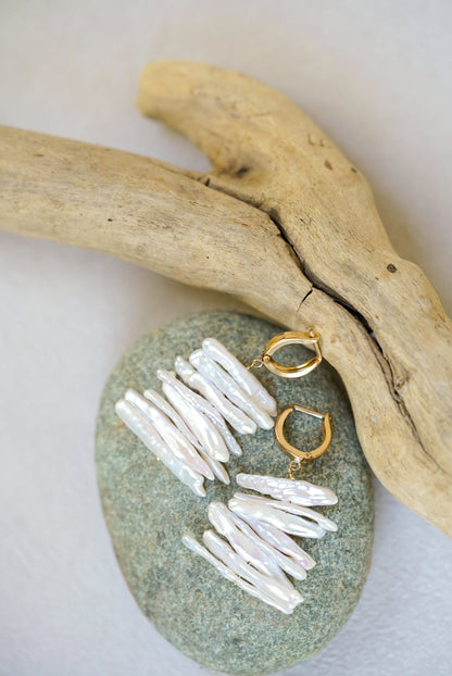 Gold and pearl earrings on a stone with driftwood