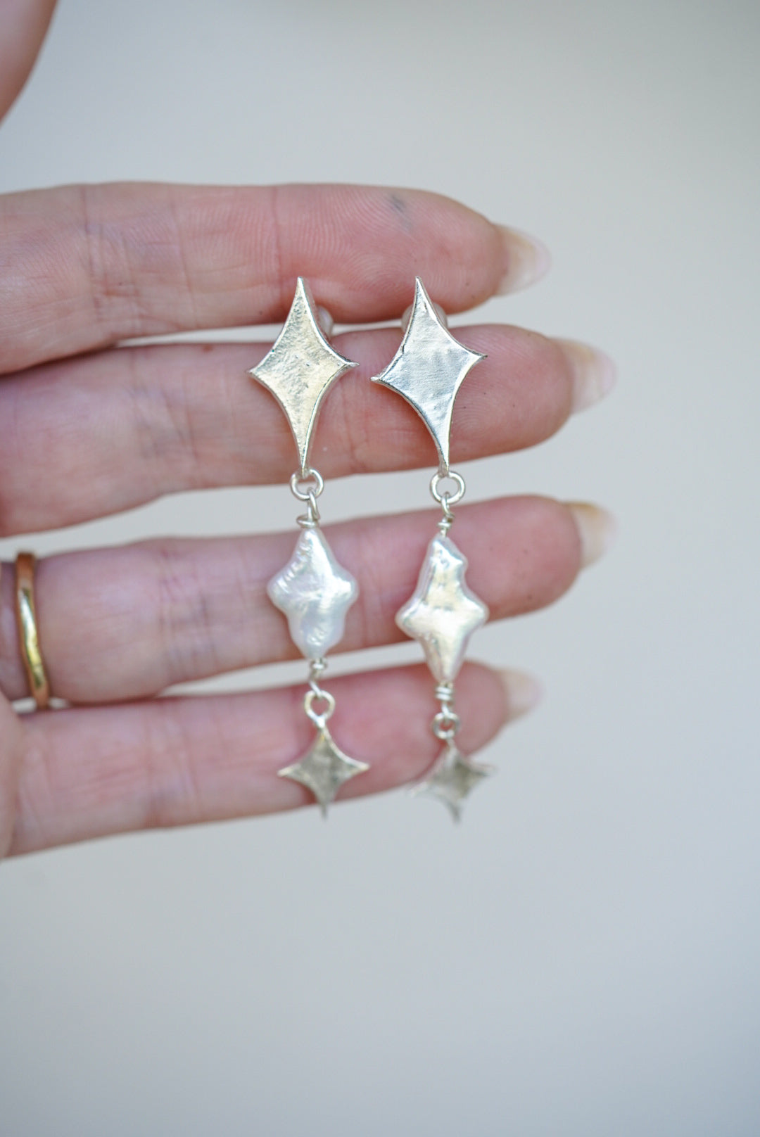 Silver star earrings held between fingers against a neutral background