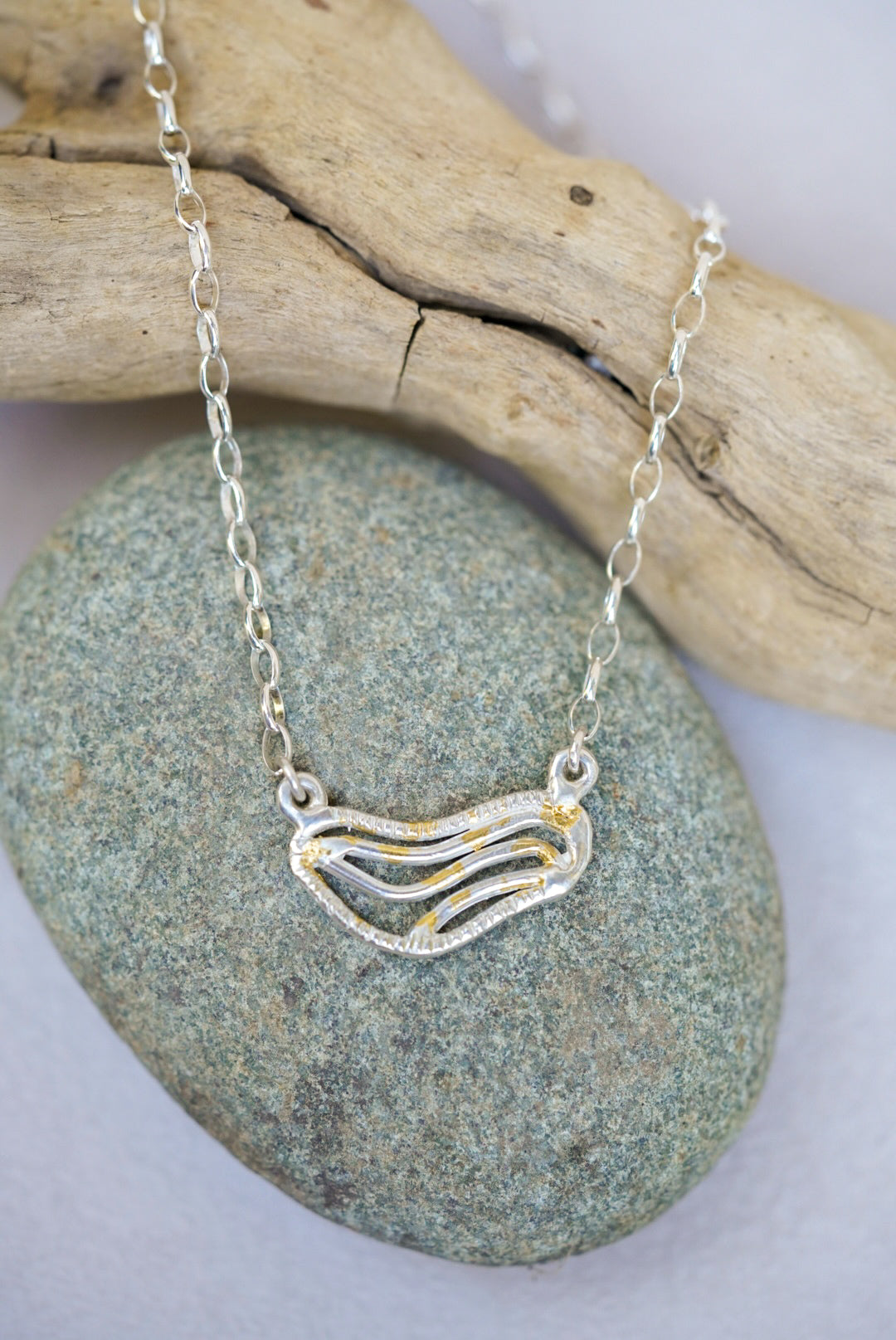 Silver necklace with a wave-shaped pendant on a stone surface