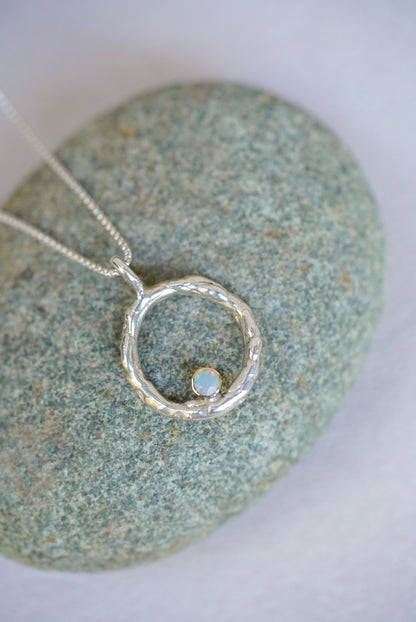 Silver necklace with a circular pendant on a textured stone surface