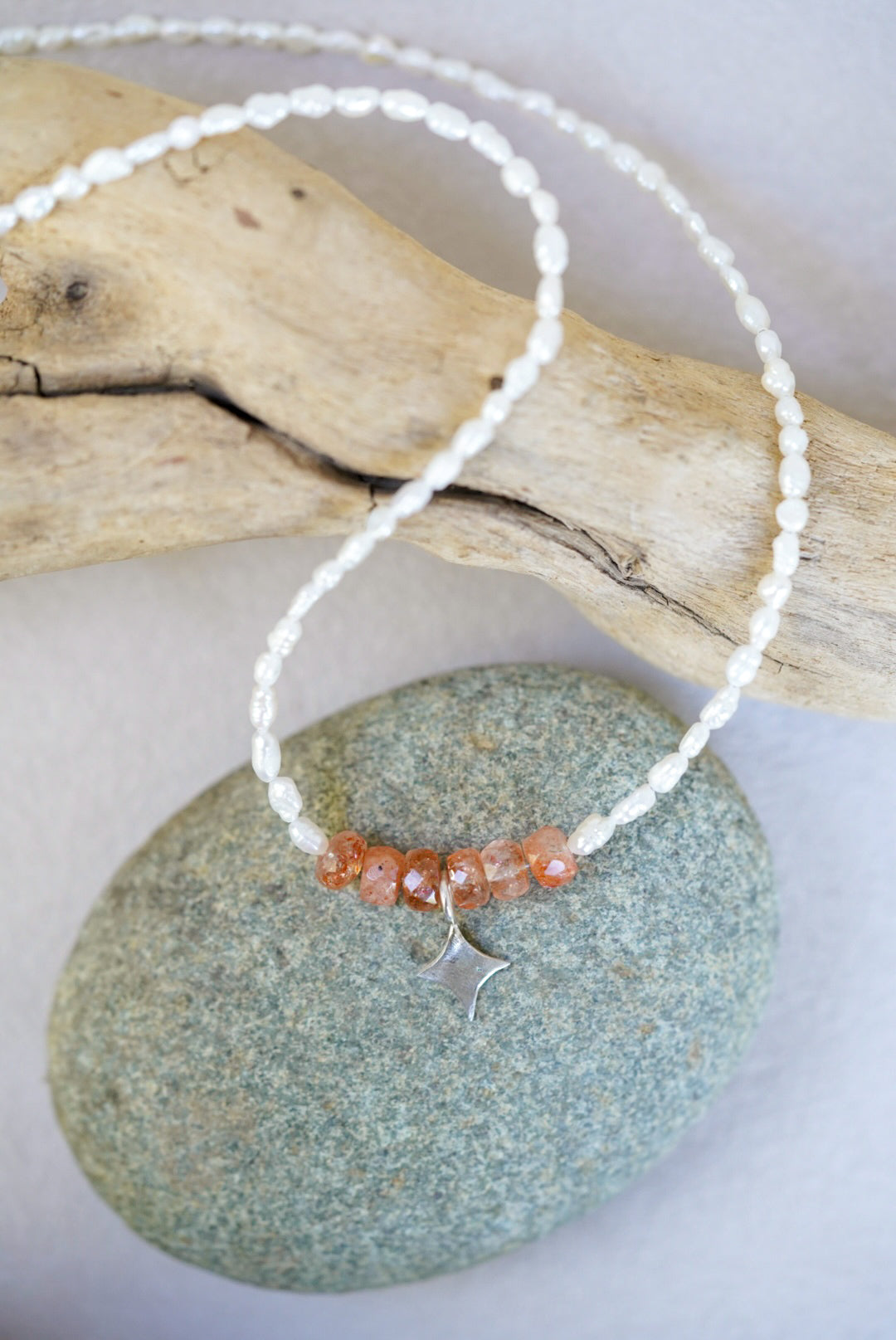Necklace with sunstone beads and a silver clasp on a stone surface with driftwood