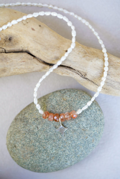Necklace with sunstone beads and a silver clasp on a stone surface with driftwood