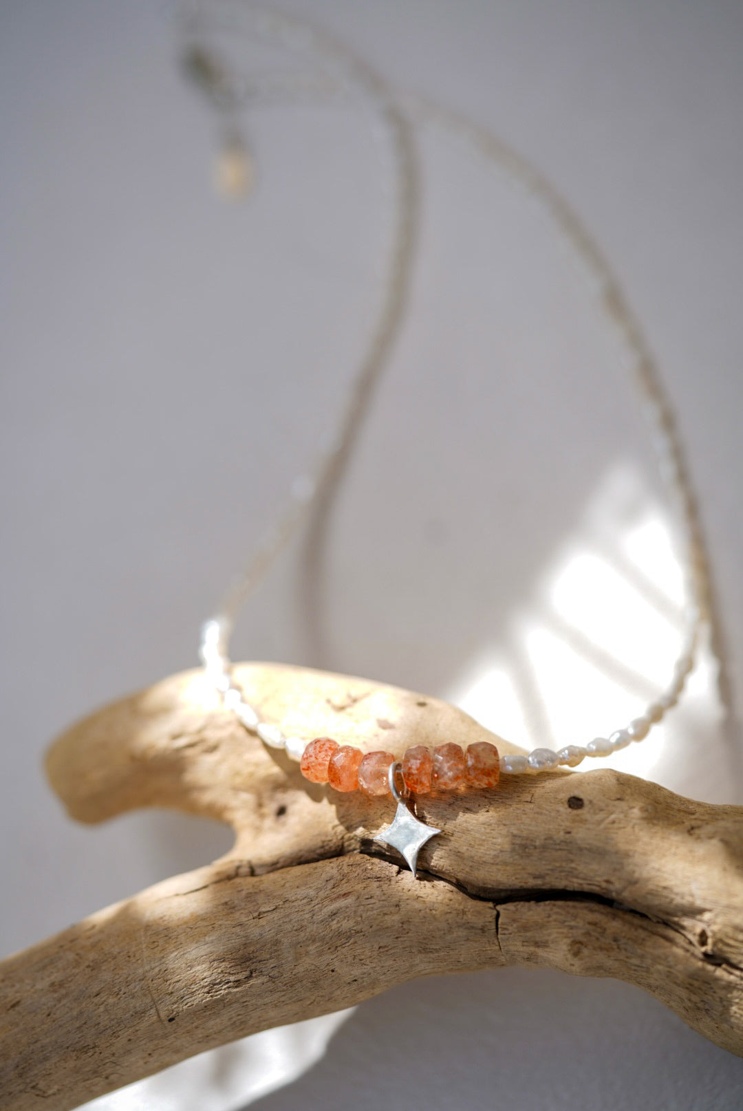 Necklace with sunstone and pearl beads on a branch against a light background
