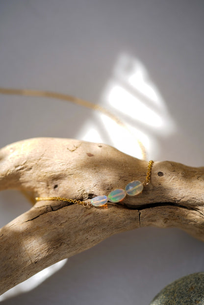 Opal necklace on a piece of driftwood with sunlight casting shadows
