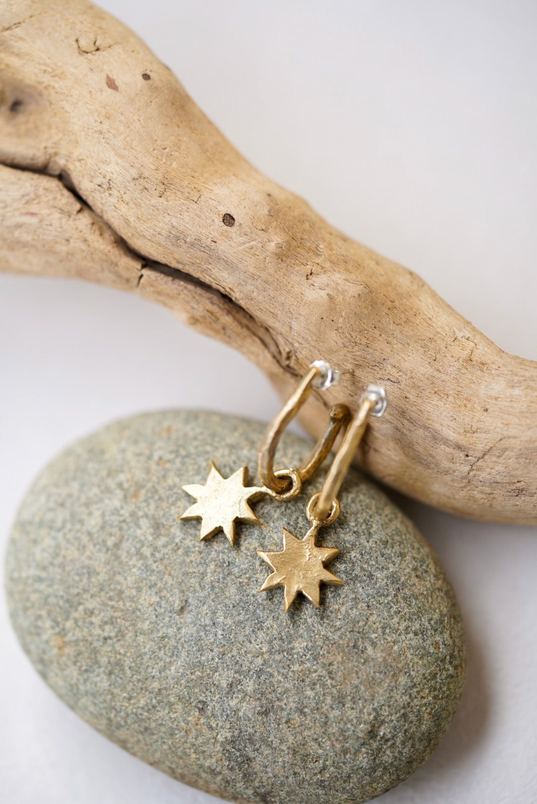 Gold star-shaped earrings on a stone with driftwood