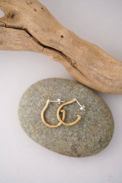 Gold hoop earrings on a stone with a wooden branch in the background