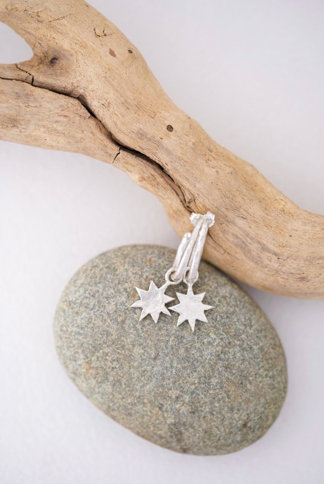 Silver star-shaped earrings on a stone with driftwood in the background