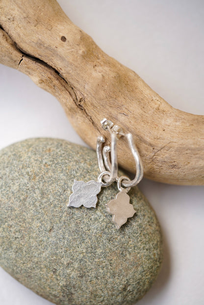 Silver earrings with charms on a piece of driftwood and stone.