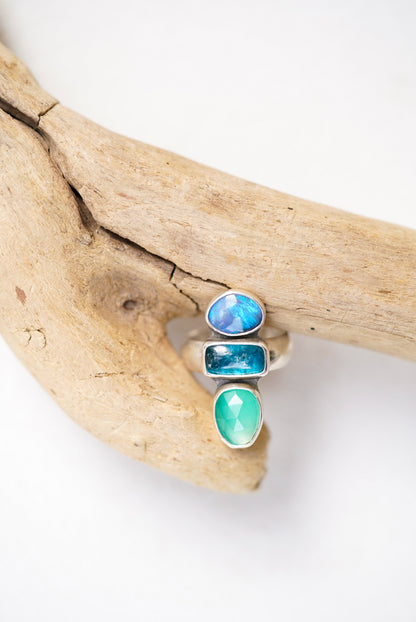 Three gemstone rings on a piece of driftwood against a white background