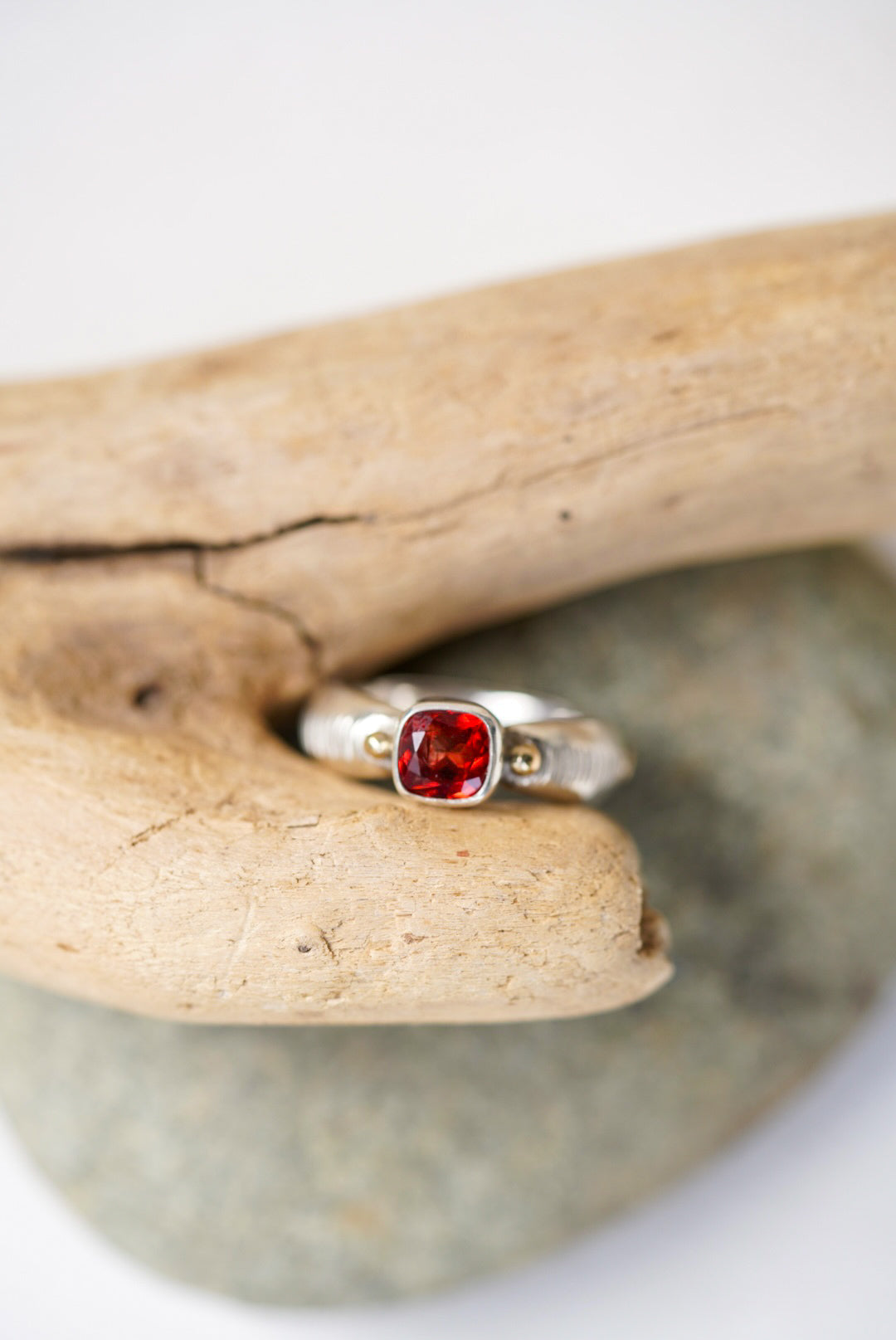 Bright red sunstone silver ring next to a piece of driftwood