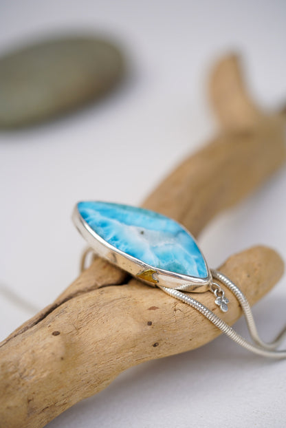 Larimar pendant on a silver chain resting on a piece of driftwood.