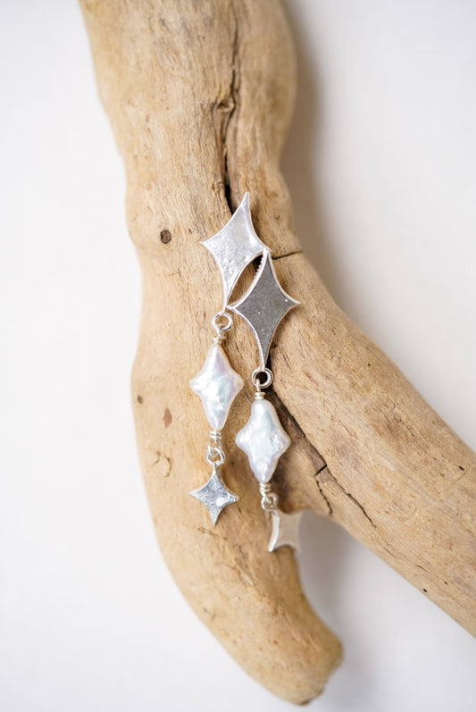 Silver earrings with star designs on a piece of driftwood.