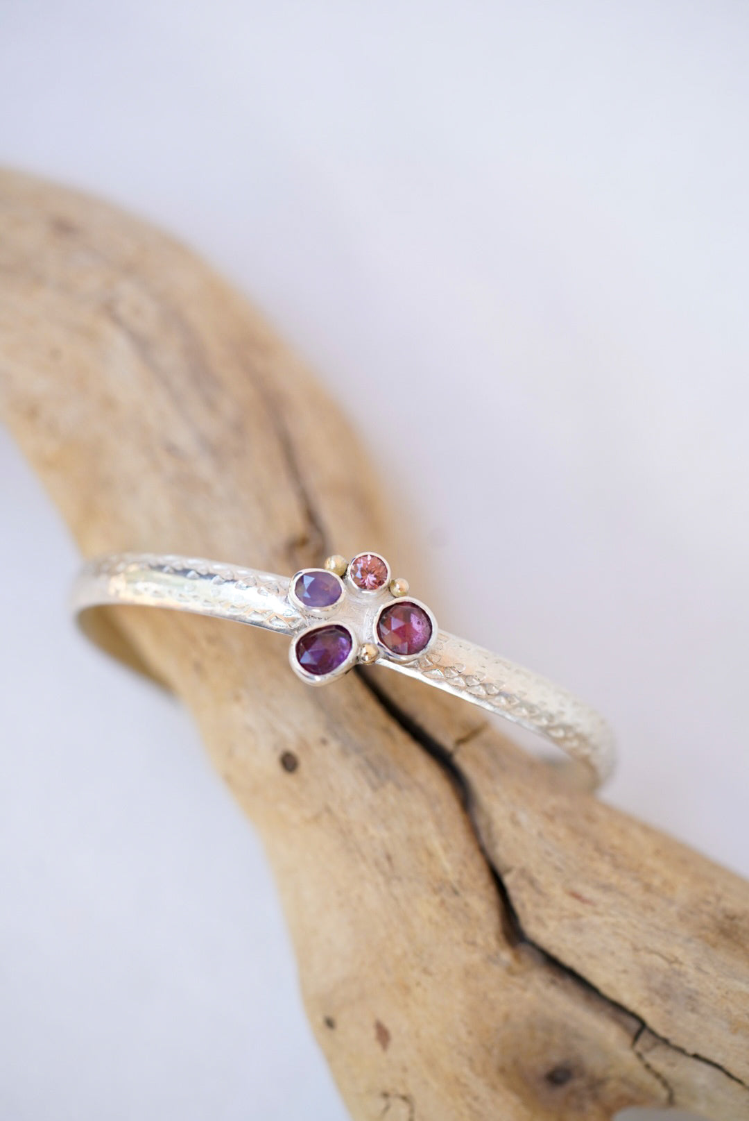 Silver cuff with purple and pink gemstones on a wooden surface 