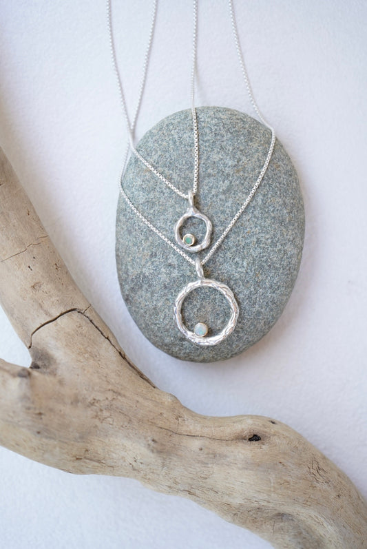 Silver necklaces with a pendant on a gray stone and wooden branch against a white background