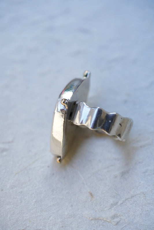A sterling silver ring with a wavy, textured band, photographed on a light textured surface.