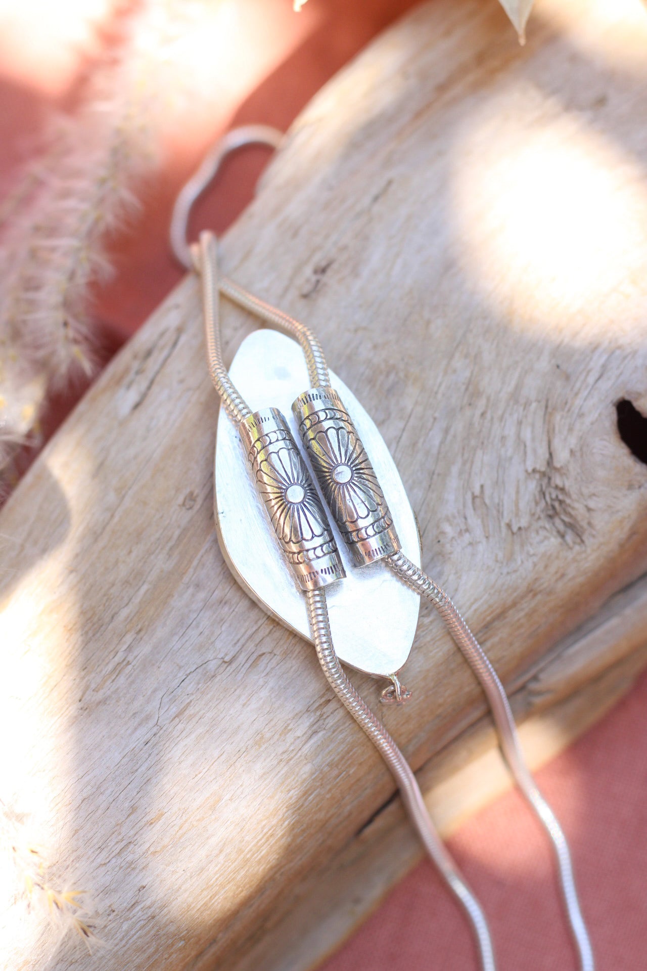 The back of a silver bolo necklace with a unique design on a wood surface