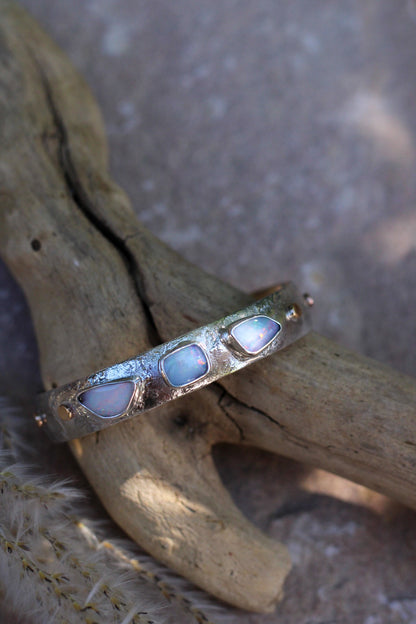 Silver bracelet with three light colored opal stones on a wooden surface